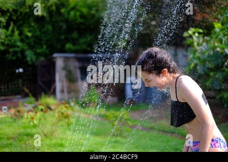 Une fille se rafraîchi pendant la vague de chaleur avec l'arroseur de jardin. 25 juin 2020 Devon Royaume-Uni Banque D'Images