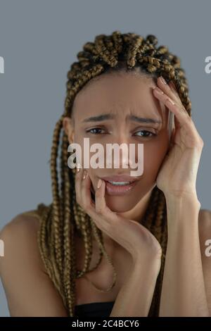 Dévasté, la jeune Afro-américaine tient le visage avec ses mains, se frognant avec douleur Banque D'Images