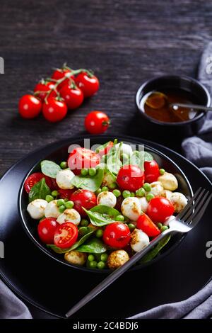 Salade de capes italienne avec pois sucriers, petits épinards, tomates cerises, mini boules de mozzarella, nappées de sauce au vinaigre balsamique servi sur un plat noir Banque D'Images