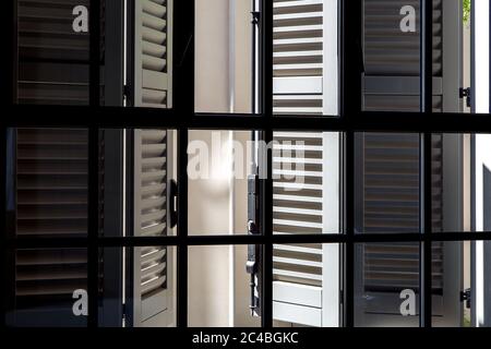 Volets en bois gris sur une vue de jour ensoleillée de l'intérieur par une fenêtre avec un cadre noir et verre, volets italiens traditionnels sur une journée ensoleillée. Banque D'Images