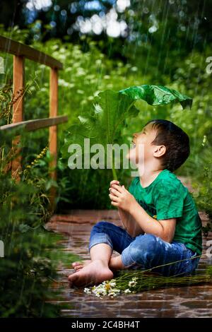 un petit garçon est assis dans la pluie et est couvert de terrier Banque D'Images