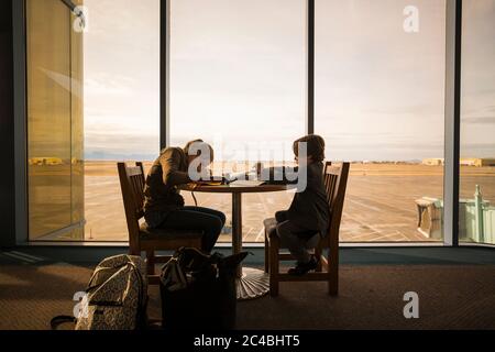 Un garçon et sa sœur aînée s'asseoir à une table dans un salon de l'aéroport, écrire et dessiner.