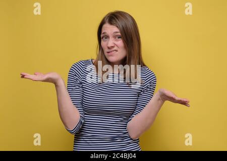 Une jeune femme attirante haussant les épaules sur un mur jaune. Banque D'Images