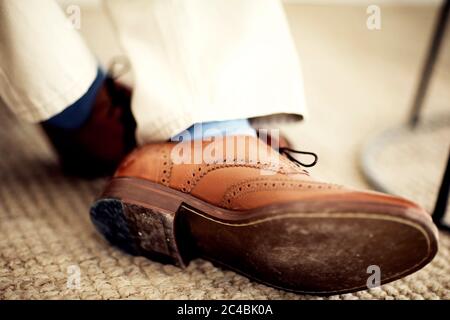 Gros plan des pieds de la personne, portant des brogues en cuir marron, des chaussettes bleues et un pantalon blanc. Banque D'Images