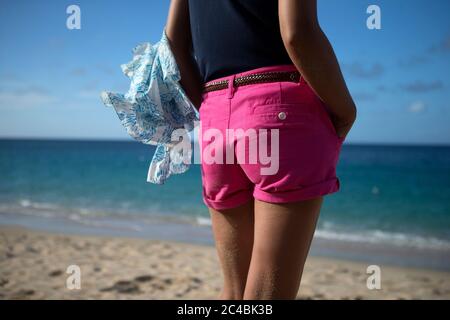 Vue arrière d'une femme portant un pantalon chaud rose sur une plage de sable au bord de l'océan. Banque D'Images