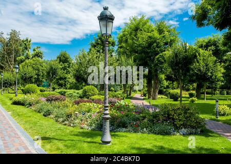 le parc a des allées et des plantes en croissance autour des massifs de fleurs et des buissons verts avec des arbres, des lampadaires en fer avec des feux de rue rétro sont installés sur le vert Banque D'Images