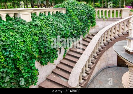 escalier en granit avec des rampes et balustrades descendant le long d'un mur de pierre avec une plante verte curly dans un jardin avec des arbres. Banque D'Images