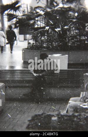 Belle photographie en noir et blanc vintage des années 1970 d'un vieil homme lisant un livre dans le centre commercial local. Banque D'Images
