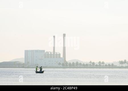 Pêcheur pêchant sur un petit canot avec cheminée d'usine sur le fond au Brésil Banque D'Images