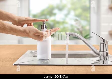 Mains de sexe masculin appuyant sur une bouteille de savon liquide à côté d'un évier dans une cuisine Banque D'Images