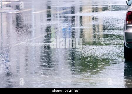 route avec des flaques d'eau sous la pluie et réflexions des bâtiments de la ville. voiture sur rue inondée. temps pluvieux dans la ville. Banque D'Images