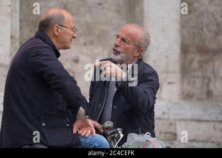 Deux hommes italiens parlent à l'autre sur la place Piazza del Popolo à Ascoli Piceno, en Italie. L'homme droit utilise un geste de la main pointant Banque D'Images