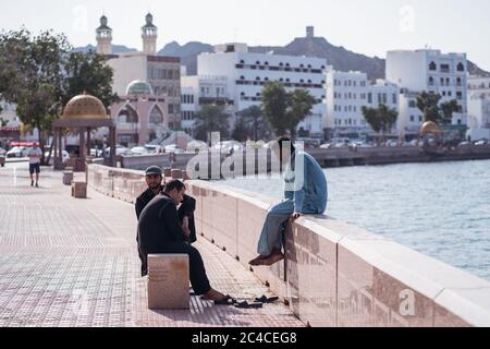 Muscat / Oman - 15 février 2020 : groupe d'amis musulmans de sexe masculin Profitez de votre temps libre assis dans la corniche de Muscat avec le Souq de Mutrah en arrière-plan Banque D'Images