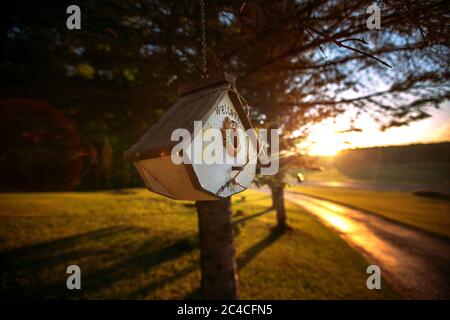 Maison Birdhouse avec un panneau de bienvenue en bois et brindilles suspendus au coucher du soleil. Banque D'Images