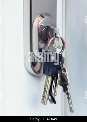 Ensemble de clés insérées dans la serrure de porte sur la porte blanche. Banque D'Images