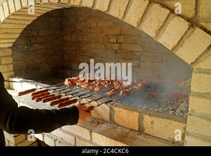 Barbecue arménien ou khorovats grillés dans un four traditionnel en argile, la main du chef se tournant une brochette dans le premier plan Banque D'Images