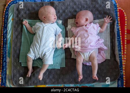 Nouveau-né garçon et fille jumeaux sur leur dos sur une sélection de tapis. Les deux bébés pleurent en raison de mannequins tombés. Photo de Sam Mellish Banque D'Images