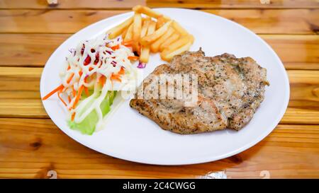 Steak de porc avec frites et salade dans une assiette blanche sur une table en bois Banque D'Images
