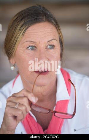 Potrait élégant femme d'affaires mature et attrayante avec des lunettes et une expression réfléchie, un arrière-plan flou. Banque D'Images