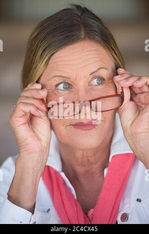 Potrait élégant mature femme d'affaires attrayante avec des lunettes et curieux intéressé expression, flou de fond. Banque D'Images