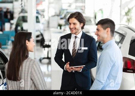 Vendeur proposant une voiture de couple debout dans la salle d'exposition Auto Banque D'Images