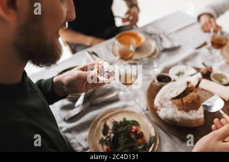 Gros plan homme assis à la table tenant une tranche de pain avec confiture et fromage à la main sur le déjeuner dans le café Banque D'Images
