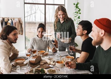 Femme souriante avec salade à la main, passant du temps avec des collègues. Groupe d'amis internationaux très intéressants assis à la table, plein de nourriture Banque D'Images