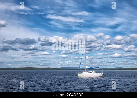 Bleu pacifique lac avec bateau avec drapeau russe dans la forêt boréale en journée ensoleillée avec de nombreux nuages magnifiques Banque D'Images