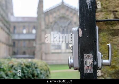 Point d'intérêt peu profond d'une porte de parc ouverte montrant un type numérique, serrure combinée, permettant aux membres du public d'accéder à une grande cathédrale. Banque D'Images