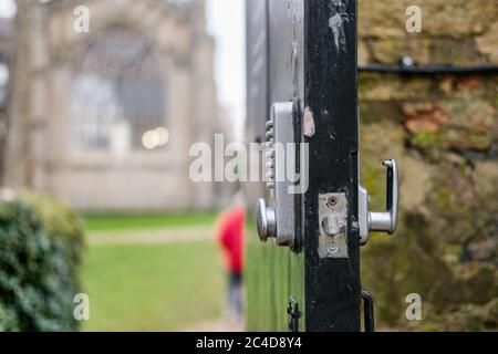 Point d'intérêt peu profond d'une porte de parc ouverte montrant un type numérique, serrure combinée, permettant aux membres du public d'accéder à une grande cathédrale. Banque D'Images