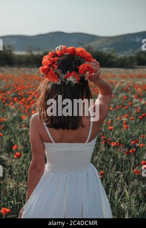 Mariée dans une robe blanche dans une couronne de coquelicots rouges, temps chaud de coucher de soleil sur le fond du grand champ de coquelicot rouge. Copier l'espace. Le concept de calme Banque D'Images
