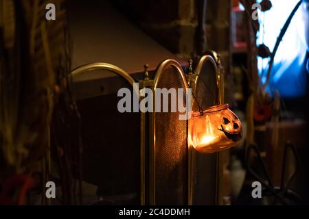 Une lanterne décorative en verre de style citrouille, isolée et peu profonde, suspendue à un garde-feu devant un feu de style ancien. Banque D'Images