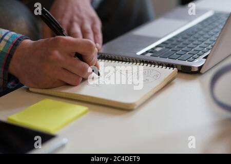 Espace de travail du jeune homme. Vue rapprochée du schéma de dessin des mains de l'homme dans l'ordinateur portable Banque D'Images