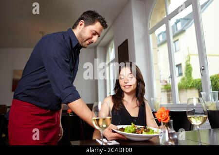 Un serveur sympathique apporte de la salade à la femme au restaurant Banque D'Images