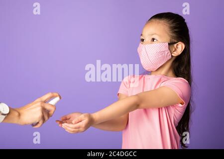 Fille dans le masque utilisant l'assainisseur isolé sur le mur violet de studio Banque D'Images