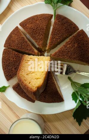 Tranché, divisé tarte éponge en portionsand une tasse de café avec du lait sur un fond en bois. Une pièce est prise et posée sur le dessus. Pose à plat. Min Banque D'Images