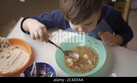 L'enfant d'âge préscolaire apprend à manger de la soupe lui-même assis à la table de cuisine. Concept de nourriture saine à la maison. Vue de dessus Banque D'Images