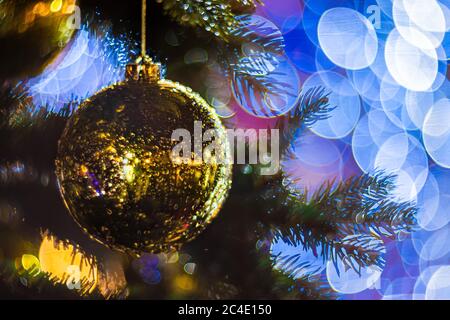 Gros plan d'un sapin de Noël à la décoration festive avec boule dorée brillante sur fond de fée étincelante. Guirlande lumineuse défocace, bokeh Banque D'Images