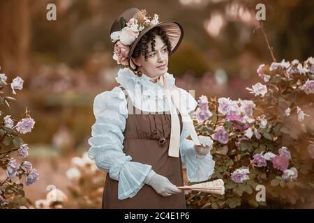 Portrait de la belle femme en plein air portant un large bord ruban cravate chapeau de paille, robe vintage. Modèle posant dans le jardin de roses en fleurs. Banque D'Images