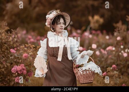 Portrait de la belle femme en plein air portant un large bord ruban cravate chapeau de paille, robe vintage. Modèle posant dans le jardin de roses en fleurs. Banque D'Images