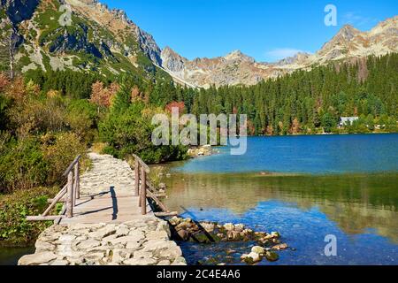 Pont en bois et passerelle en pierre au lac de Poprad d'automne avec des sommets et des forêts colorées près du parc national de High Tatras, Slovaquie Banque D'Images