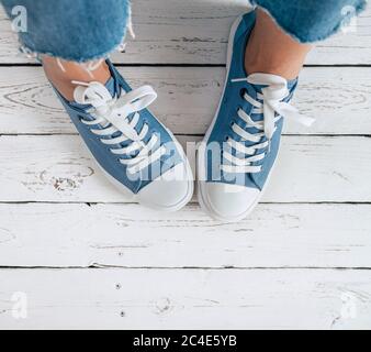 Les pieds de l'adolescent de couleur bleue décontracté nouvelles baskets avec lacets blancs sur le sol blanc image gros plan. Style vintage dans le monde de la mode moderne Banque D'Images