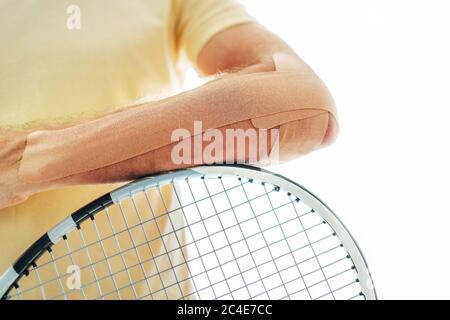 Coude de joueur de tennis avec bande élastique thérapeutique ou Kinesio appliquée sur le bras allongé sur la raquette à l'image de près de la salle orthopédique. peo sport actif Banque D'Images
