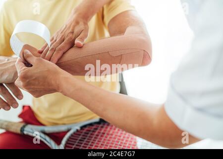 Coude de joueur de tennis avec bande élastique thérapeutique ou Kinesio appliquée par l'infirmière à l'image rapprochée du service orthopédique. Active sportive personnes santé reh Banque D'Images