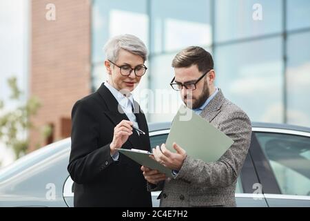 Les gens d'affaires debout à l'extérieur lisant le contrat ensemble et en discutant Banque D'Images
