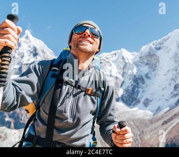 Portrait de l'homme de Hiker souriant sur Taboche 6495m et Cholatse 6440m pics fond avec des bâtons de trekking, UV protégeant des lunettes de soleil. Il appréciant la montagne Banque D'Images