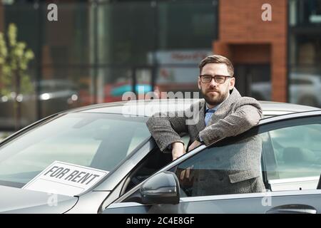 Portrait d'un homme d'affaires à barbe mûr en lunettes regardant l'appareil photo tout en se tenant près de la voiture à l'extérieur Banque D'Images