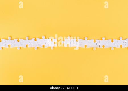 Rangée de pièces de puzzle blanches perturbées avec lien manquant sur fond jaune Banque D'Images