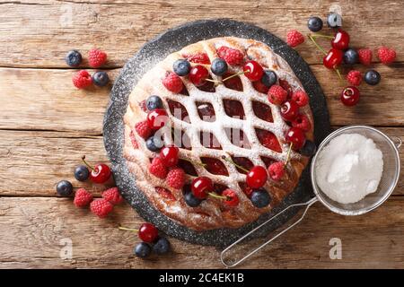 tarte crostata aux framboises, bleuets et cerises arrosées de sucre en poudre sur un panneau d'ardoise sur la table. vue horizontale du dessus de Banque D'Images