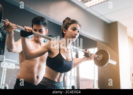 Entraîneur personnel aidant les femmes et de manipuler les cloches lourdes deux mains haut un épaule dans la salle de gym. Banque D'Images